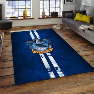 May include: A rectangular blue rug with two white stripes running down the center. The rug features the Ravenclaw crest, with a blue shield, a raven, and the words "Ravenclaw" in gold.