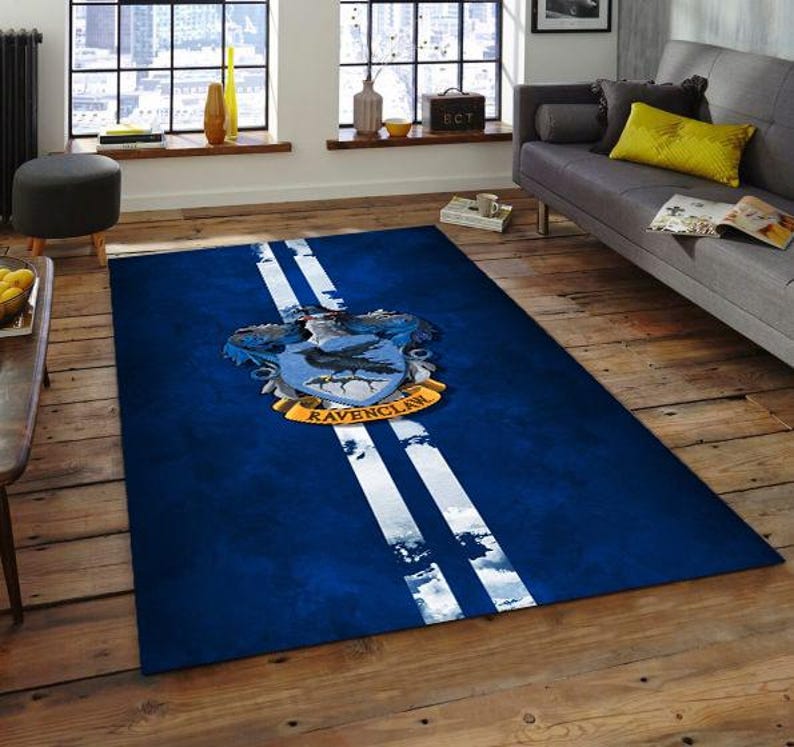May include: A rectangular blue rug with two white stripes running down the center. The rug features the Ravenclaw crest, with a blue shield, a raven, and the words "Ravenclaw" in gold.