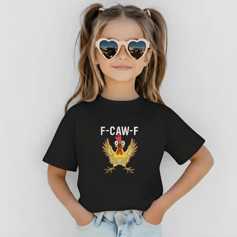 K&ouml;nnte beinhalten: Ein schwarzes T-Shirt mit dem Text "F-CAW-F" und einem Cartoon-H&uuml;hner-Design. Das Huhn ist gelb, rot und braun. Die Person auf dem Bild tr&auml;gt herzf&ouml;rmige Sonnenbrillen.
