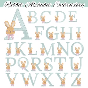 Op de afbeelding: Een alfabetborduurset met de tekst "Rabbit Alphabet Embroidery". Elke letter is lichtblauw en heeft een klein, geborduurd konijn met een roze strik. De letters zijn in een schreeflettertype.