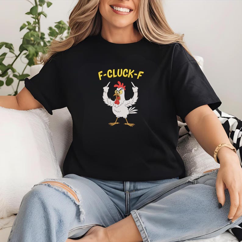 K&ouml;nnte beinhalten: Schwarzes T-Shirt mit einer humorvollen Grafik eines wei&szlig;en Huhns, das den Mittelfinger zeigt, mit dem Text "F-CLUCK-F" in Gelb. Das Huhn hat einen roten Kamm und gelbe F&uuml;&szlig;e. Das T-Shirt wird von einer Person getragen.