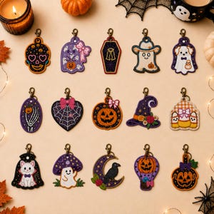 May include: A collection of fifteen embroidered Halloween-themed keychains featuring various designs including a skull, ghosts, a coffin, a pumpkin, a witch hat, a skeleton hand, a cat, a mushroom, a crow on a moon, and a hot air balloon.
