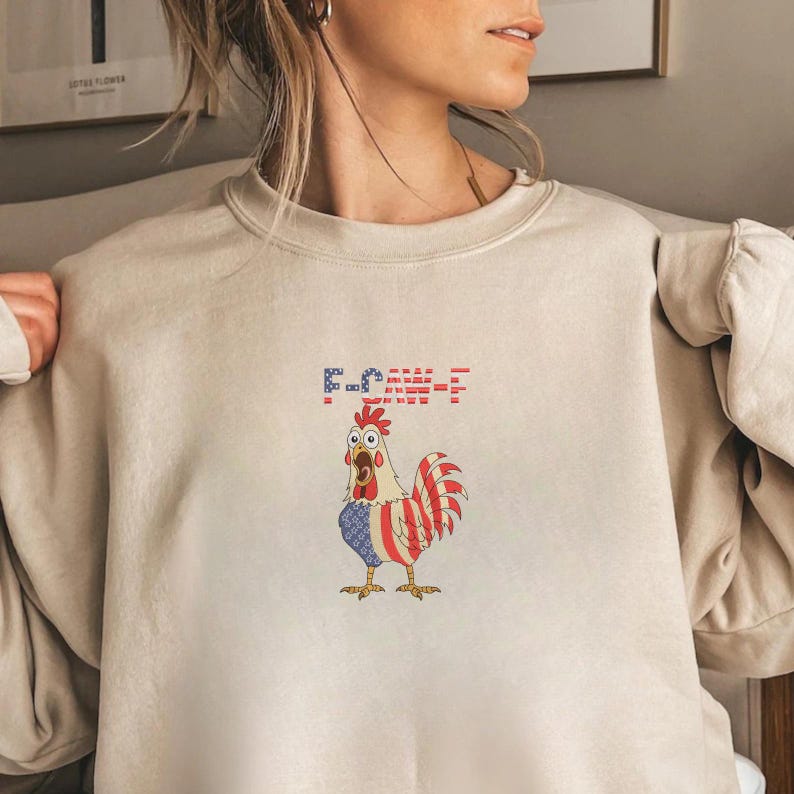 K&ouml;nnte beinhalten: Beiges Sweatshirt mit einem Cartoon-Hahn in Rot, Wei&szlig; und Blau, &auml;hnlich der amerikanischen Flagge. Der Text "F-CK-E-F" befindet sich &uuml;ber dem Hahn. Ein bequemes, l&auml;ssiges Kleidungsst&uuml;ck.