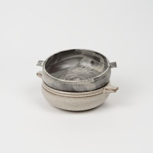 May include: A set of three ceramic mugs with a speckled, matte finish. Each mug features a different color: light blue, cream, and gray. The mugs have a simple, modern design and a comfortable handle.