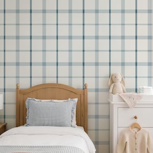 May include: A bedroom scene featuring a light wood bed frame with a blue and white gingham pillow and white bedding. The wall is covered in wallpaper with a blue and white plaid pattern. A white dresser holds a plush rabbit and a beige cardigan.