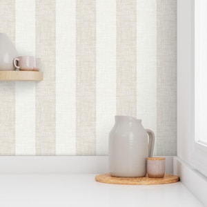 May include: A white and beige striped wallpaper with a textured linen look. A gray ceramic pitcher and a small gray ceramic jar are sitting on a wooden tray.