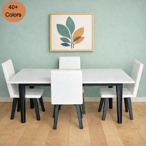 May include: A modern dining set with a white tabletop and four white chairs. The table has black legs. A framed artwork with green and orange leaf design hangs on the light green wall. The image includes the text "40+ Colors" in a circle.