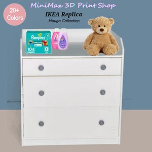 Puede incluir: Una cómoda blanca de tres cajones con pomos grises, que contiene productos para bebés. Una caja de pañales Pampers, dos botellas de jabón para bebés y un oso de peluche encima. El texto "MiniMax 3D Print Shop" e "IKEA Replica" son visibles.