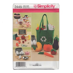 May include: A Simplicity 2445 sewing pattern envelope featuring illustrations of fabric play food items including a green tote bag with a recycle symbol, various fruits, vegetables, eggs in a carton, a small pink pot, and cupcakes on stands.