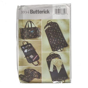 May include: A Butterick sewing pattern featuring various travel bags and garment bags. The bags are made of a dark fabric with a floral pattern. The pattern includes a duffel bag, a hanging garment bag, and a cosmetic bag.