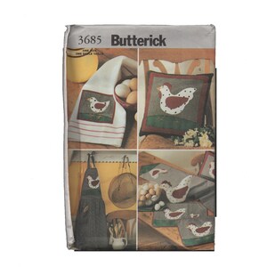 May include: A multi-panel image of a Butterick pattern featuring a chicken motif. The pattern includes designs for a kitchen towel, pillow, apron, and other kitchen textiles. The chicken design is red and white, set against a green and brown background.