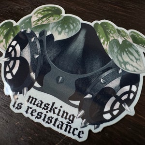 May include: A black and white sticker with a gas mask and leafy plants. The text "masking is resistance" is written in a gothic font.