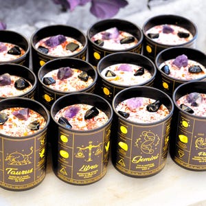 May include: Twelve black glass candle jars with gold zodiac symbols and amethyst crystals. The candles are arranged in three rows of four. The zodiac signs are Taurus, Libra, Gemini, and Pisces.