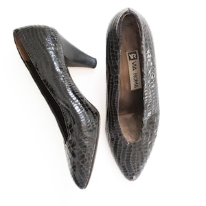Puede incluir: Un par de zapatos de tacón negros Via Roma con un patrón texturizado similar al de un reptil. Los zapatos tienen puntas afiladas y tacones pequeños. El interior de un zapato muestra una etiqueta Via Roma.