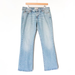 Peut inclure: Un jean en denim bleu clair suspendu à un cintre en bois. Le jean a une conception classique à cinq poches, une fermeture à bouton et à glissière, et une légère ouverture de jambe évasée. Le jean est de couleur moyenne avec une décoloration subtile.