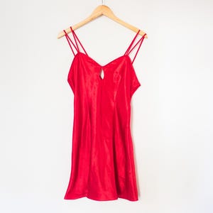 May include: A red satin slip dress with adjustable straps and a keyhole opening at the neckline.