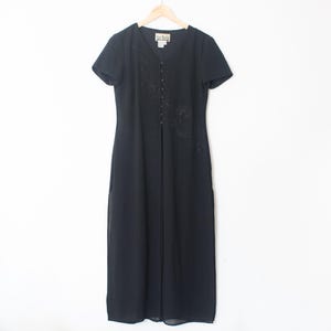 Puede incluir: Un vestido maxi negro con mangas cortas y cierre de botones en la parte delantera. El vestido tiene un delicado diseño floral bordado en la parte delantera.