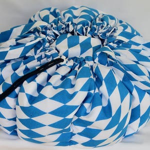 Peut inclure: Un sac de rangement rond à cordon de serrage avec un motif de losanges bleus et blancs. Le sac a deux poignées et une fermeture à cordon noire. Le tissu est froncé en haut, créant une forme bouffante.