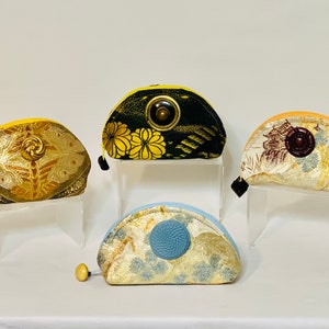 May include: Four half-circle shaped pouches with gold and silver fabric and decorative buttons. The pouches are displayed on clear acrylic stands.
