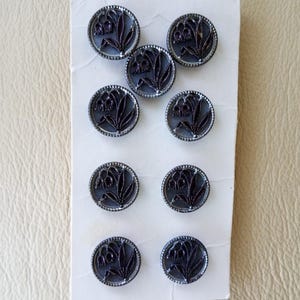May include: A pack of ten black and silver buttons with a floral design. The buttons are round and have a raised design of a flower with a stem and leaves.