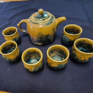 May include: A yellow and blue ceramic teapot and six matching teacups. The teapot and cups have a floral design with black outlines.