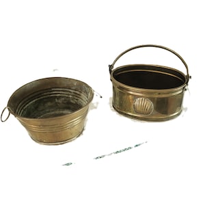 May include: Two brass buckets, one with a handle and a shell design, the other without a handle.