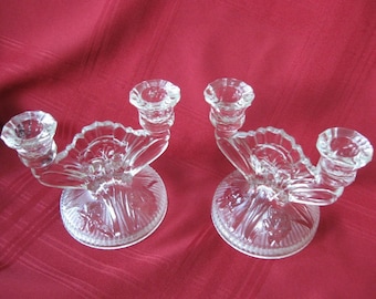 May include: A pair of clear glass candle holders with a floral design. Each holder has two candle cups and a wide base.