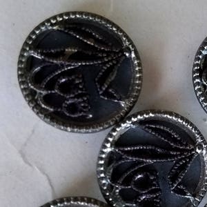 May include: A set of six silver-toned buttons with a black, intricate design. The buttons have a raised, circular rim and a flat center.