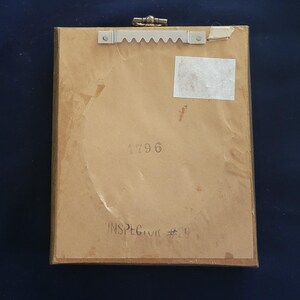May include: The back of a framed picture with a brown wooden frame. The back of the picture has a white sticker with the number 2796 printed on it. The text "INSPECTOR #29" is printed in black ink on the back of the picture.