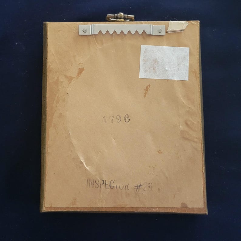 May include: The back of a framed picture with a brown wooden frame. The back of the picture has a white sticker with the number 2796 printed on it. The text "INSPECTOR #29" is printed in black ink on the back of the picture.
