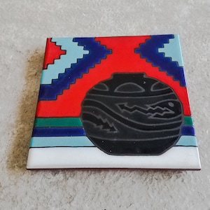 May include: A square ceramic tile with a red, blue, green, and white geometric pattern. A black ceramic pot with a stylized design is centered on the tile.