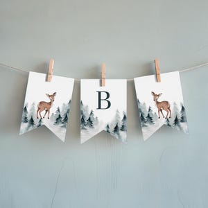 May include: A white banner with a watercolour winter forest scene and a deer. The banner has the letter "B" on it. The banner is strung with clothes pegs.