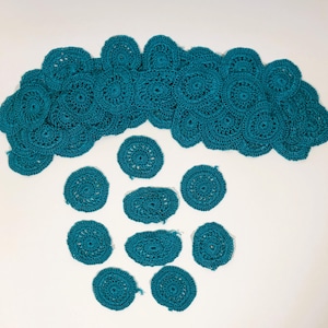 May include: A collection of teal crocheted doilies arranged in a cloud shape with smaller doilies scattered below.