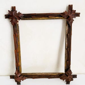 Pode incluir: Uma moldura quadrada de madeira com um design rústico. A moldura é principalmente castanha com detalhes dourados e vermelhos. Cada canto apresenta um desenho de folha esculpida. A moldura está vazia, pronta para uma foto ou obra de arte.