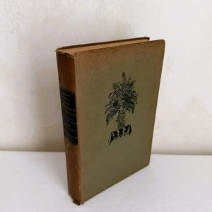 Puede incluir: Un libro antiguo con una cubierta beige descolorida y una ilustración floral negra. El lomo tiene una etiqueta negra con texto blanco. Los bordes del libro están desgastados, lo que sugiere edad. La estética general es vintage y clásica.