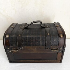 May include: A small, vintage-style chest with a plaid pattern on the top and a dark brown finish. The chest has a curved top, a handle, and metal accents. The dimensions are approximately 10 inches wide, 6 inches high, and 6 inches deep.
