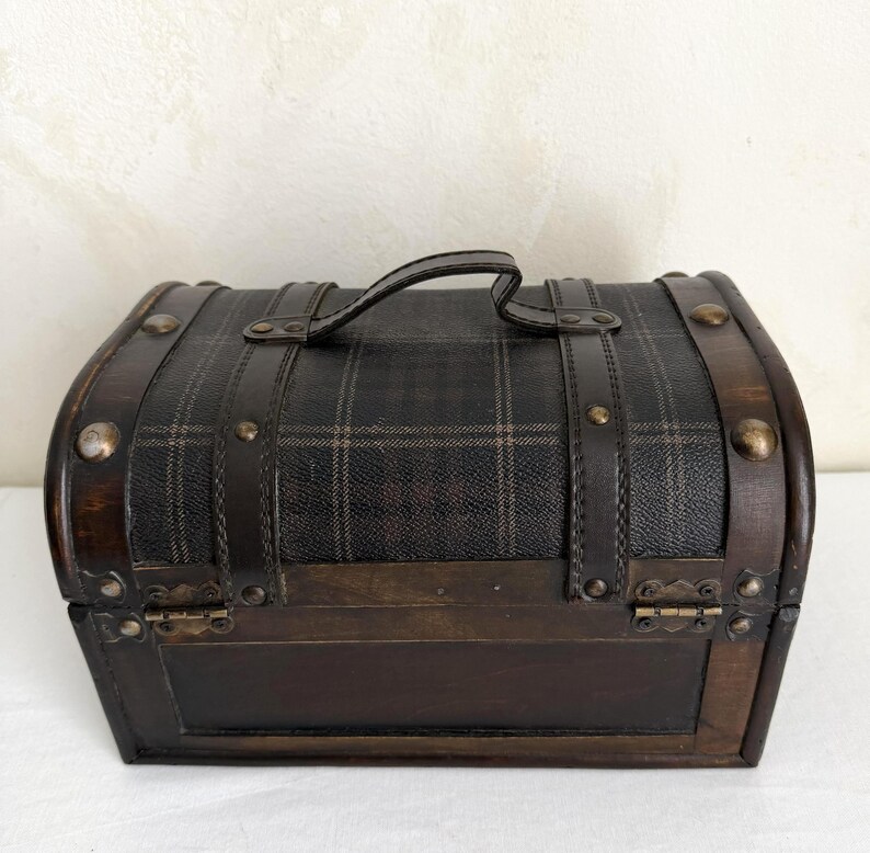 May include: A small, vintage-style chest with a plaid pattern on the top and a dark brown finish. The chest has a curved top, a handle, and metal accents. The dimensions are approximately 10 inches wide, 6 inches high, and 6 inches deep.