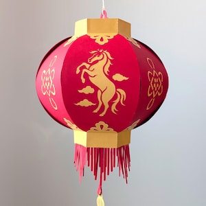 以下が含まれることがあります： 金色の装飾とフリンジが付いた赤い紙提灯。提灯の前面には、雲のある金色の馬のデザインがあります。上部と下部は金色で、白い紐で吊り下げられています。装飾品です。