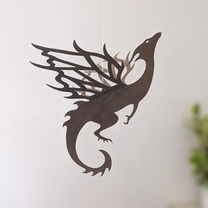 May include: A brown paper dragon mobile hanging from a white string. The dragon has intricate cut-out details and is suspended in mid-air.