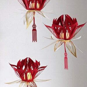 Three red and gold 3D paper lotus lanterns hanging on a wall, each glowing with an LED tealight; made from an SVG file for Cricut crafts.