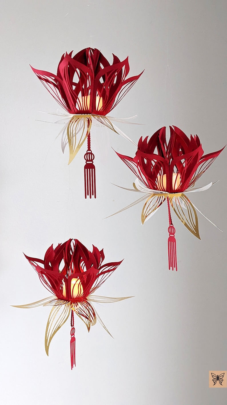 Three red and gold 3D paper lotus lanterns hanging on a wall, each glowing with an LED tealight; made from an SVG file for Cricut crafts.