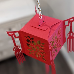 Top view of a red paper Chinese lantern showing the hanging tab, floral cutout panels, and tassel details, assembled from a 3D SVG template.