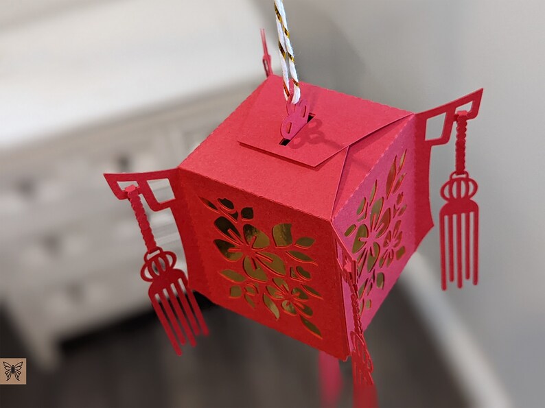 Top view of a red paper Chinese lantern showing the hanging tab, floral cutout panels, and tassel details, assembled from a 3D SVG template.