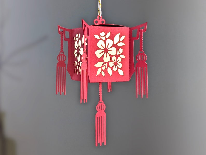 Red paper Chinese lantern with floral cutouts and hanging tassels, designed as a 3D SVG Cricut project for Lunar New Year décor.