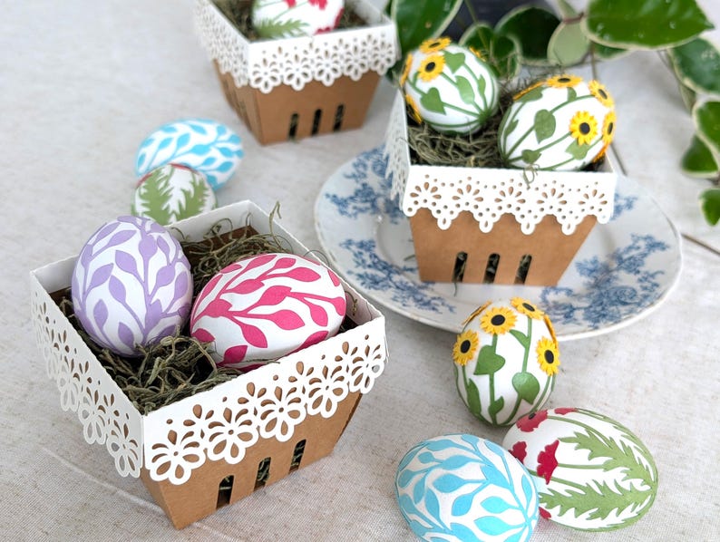 Decorative paper Easter egg wraps in pastel leaf, sunflower, and poppy designs displayed in white lace berry baskets on a spring table setting.