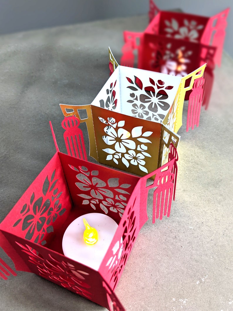 Row of red and gold paper Chinese tea light holders with floral cutouts and tassels, each crafted from SVG templates and lit with small LED candles.