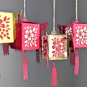 Group of red and gold paper Chinese lanterns with floral cutouts and tassel details, created from SVG files for Cricut and Lunar New Year hanging décor.