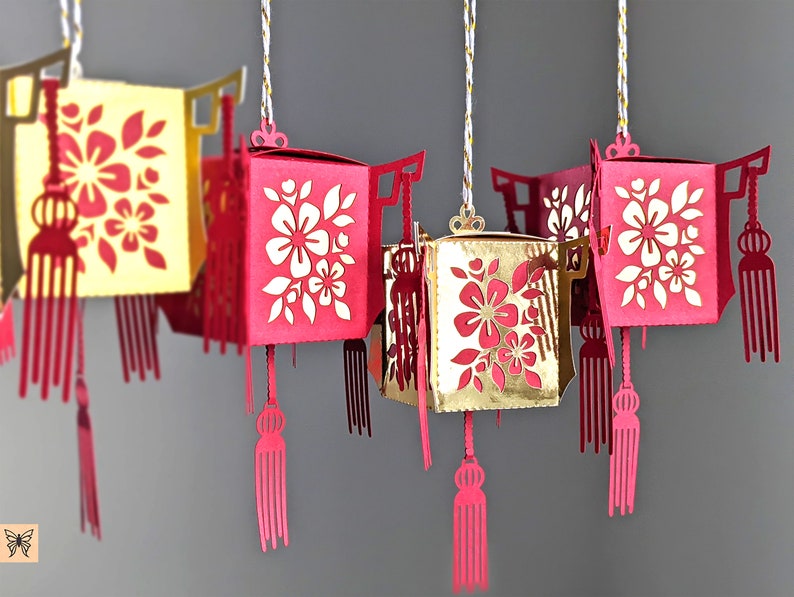 Group of red and gold paper Chinese lanterns with floral cutouts and tassel details, created from SVG files for Cricut and Lunar New Year hanging décor.
