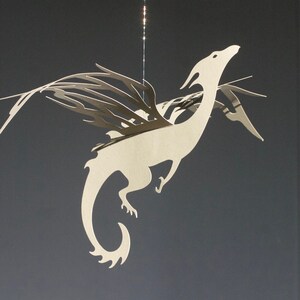 May include: A white paper dragon mobile with intricate wings and a curled tail. The dragon is suspended from a string and appears to be flying.