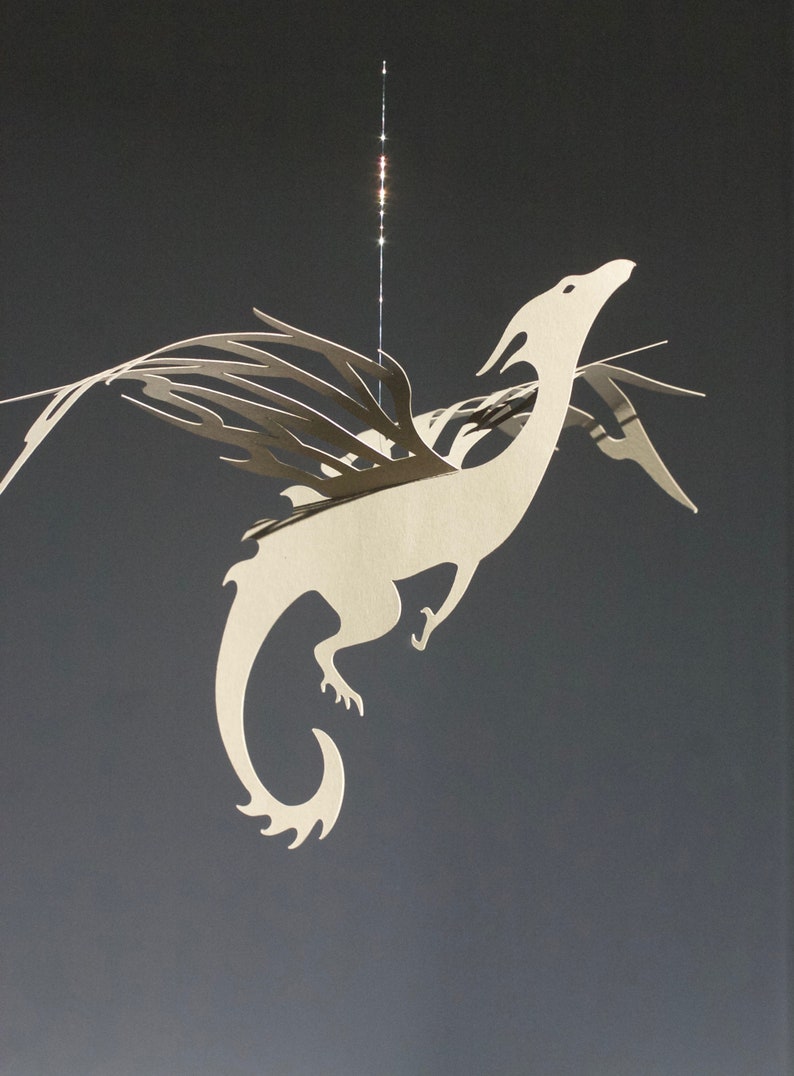 May include: A white paper dragon mobile with intricate wings and a curled tail. The dragon is suspended from a string and appears to be flying.
